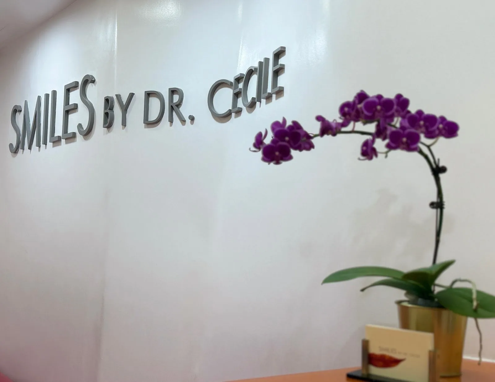 The Smiles By Dr. Cecile wordmark on the reception wall beside an orchid arrangement